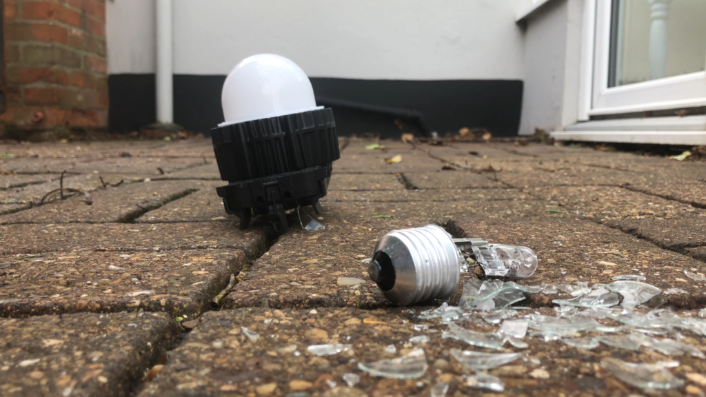 Perfectly intact Greengage ALIS lightbulb on paving stones next to a crushed glass dome consumer grade lightbulb
