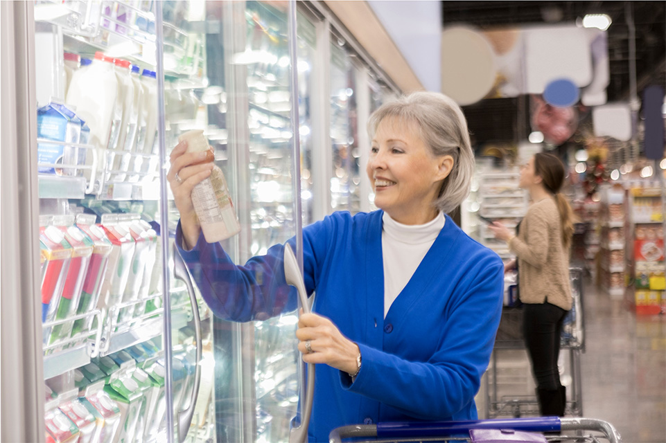 Woman taking a bottle of dairy product from a supermarket shelf and smiling at upon seeing something on the label